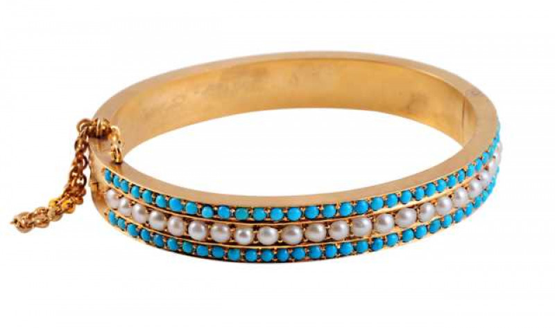 A Victorian pearl and turquoise bangle, circa 1880, the row of twenty four pearls claw set between two rows of thirty five claw set turquoise highlights. Integral tongue clasp with safety chain. Weight approx. 22.4gms. Width approx. 6cm.