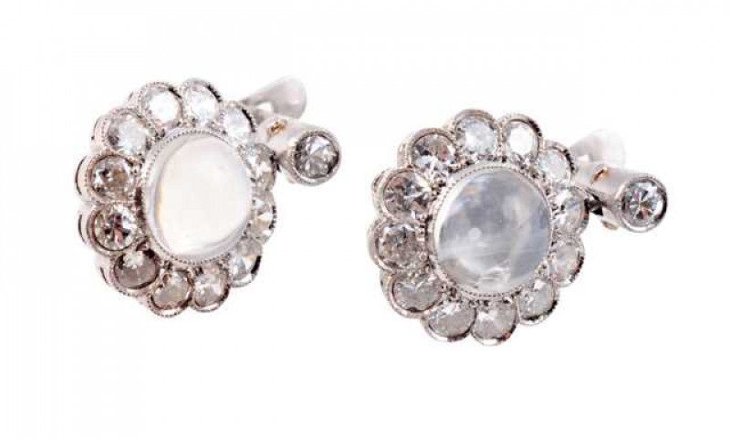 A pair of moonstone and diamond earrings, the round cabochon cut moonstone millegrain set within a bezel of twelve brilliant cut diamonds, all set in an open mount suspending from a single brilliant cut collet set diamond mount on post and guard fittings.