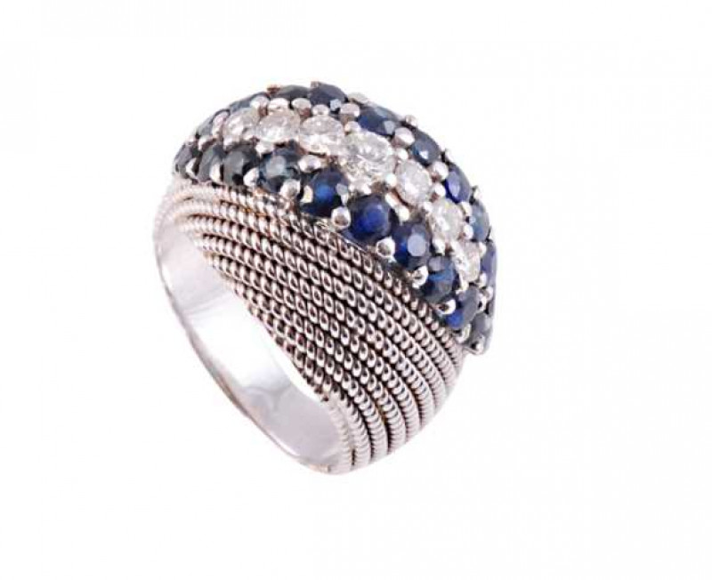 A sapphire and diamond ring, the unusual textured mount design set to the top with seven graduating brilliant cut claw set diamonds within a surround of twenty two round cut claw set sapphires, all set in an open mount on tapering shoulders. Stamped 750. 
