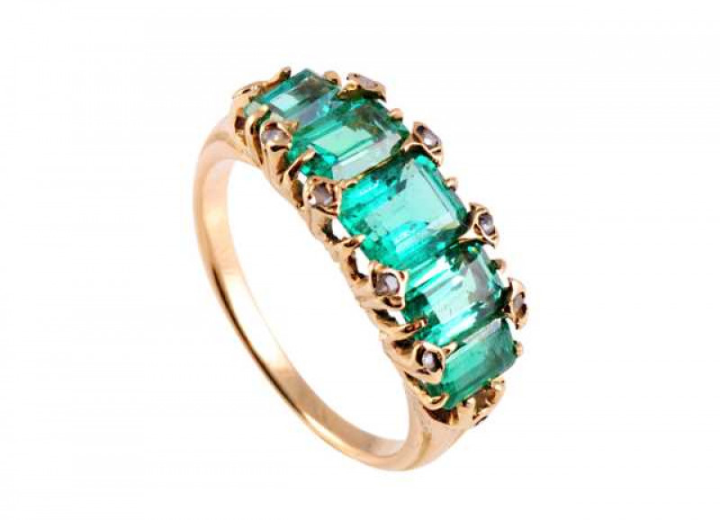 A five stone emerald ring, the central square cut emerald claw set between two rectangular cut emeralds and two further smaller square cut emeralds to each end, all claw set, every two claws more heavy and elaborate and set with a single diamond highlight