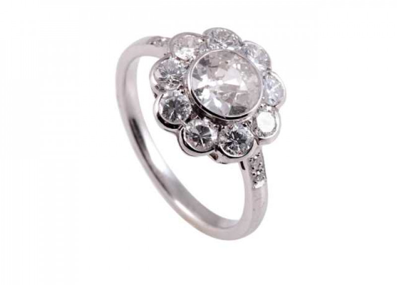 A diamond ring, the central old brilliant cut diamond collet set within a bezel of nine brilliant cut diamonds, collet set to form a flowerhead shape, all set in an open mount between shoulders each set with two diamond highlights, on a plain band. Ring s