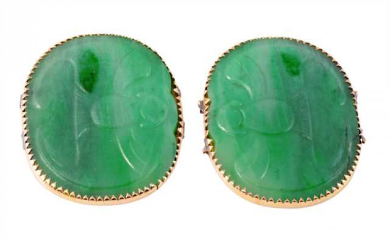 A pair of jadeite plaques, each oval plaque subtly carved with a winged figure, set in thin shaped collet settings. Both plaques weigh approx. 9.4gms. Width of one plaque approx. 3.1cm.