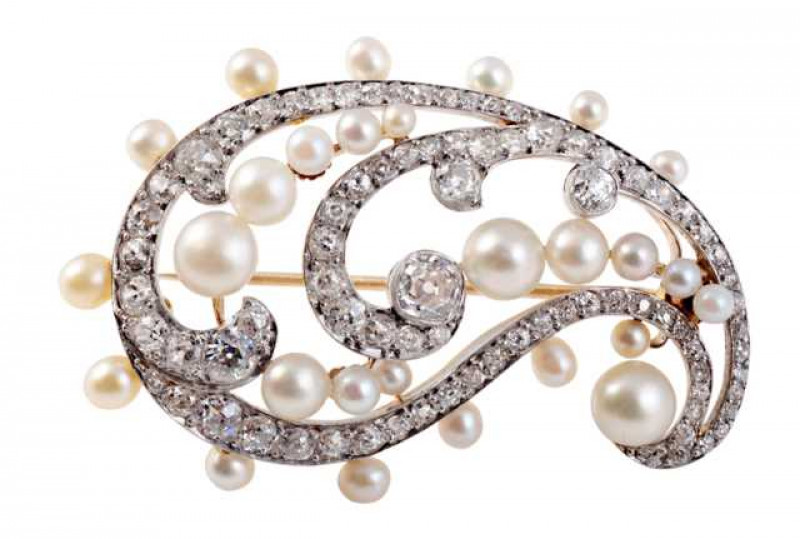 A late Edwardian pearl and diamond brooch, the delicate swirl design set throughout with graduating round mixed cut claw set diamonds and graduating natural pearls, the pearls in three clusters to the inner trefoils and evenly spaced around the outer edge