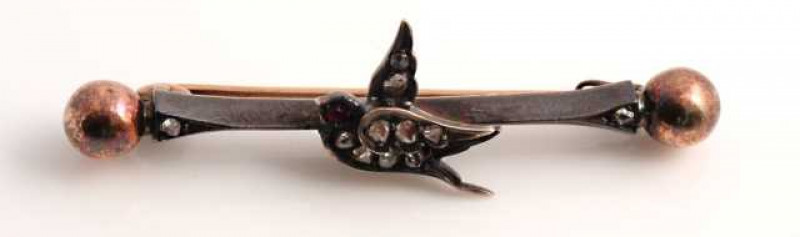 A late Victorian diamond and ruby brooch, modelled as a bird, simply set with nine rose cut diamonds to the wings and body and a single ruby highlight for the eye, set to the centre of a moulded bar with a single old cut diamond highlight to each end with