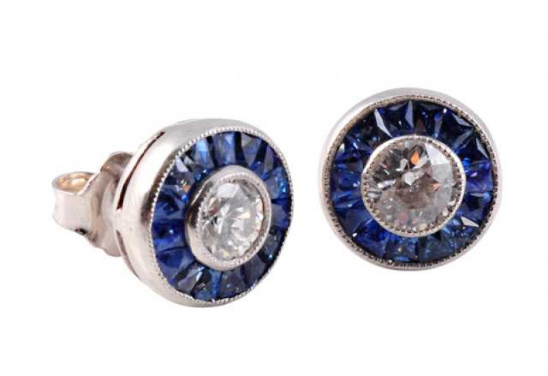 A pair of sapphire and diamond ear studs, the central brilliant cut diamond millegrain set within a bezel of fifteen square cut sapphire highlights, all in a pierced open mount on post and scroll fittings. Weight of one earring approx. 1.5gms.