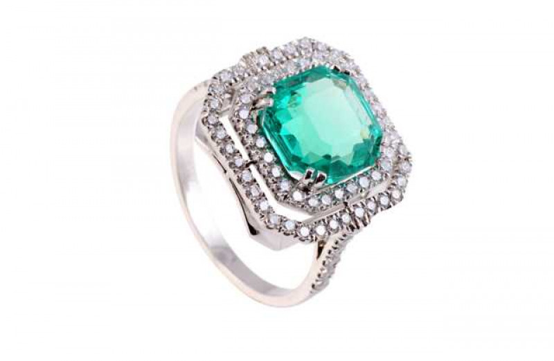 An emerald and diamond ring, the central step cut cut emerald four double claw set within an inner bezel of twenty nine brilliant cut claw set diamonds, in turn set within an outer bezel of thirty seven brilliant cut claw set diamonds, all set in an open
