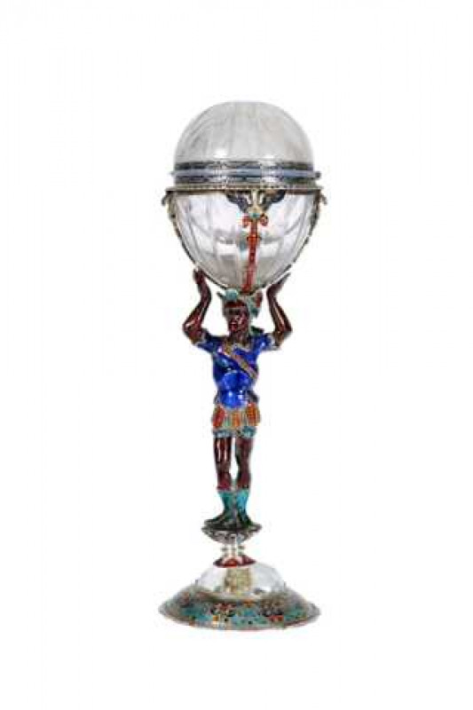 A 19th Century Austrian enamel and rock crystal figural vinaigrette, in the form of a Blackamoor, the figure holding aloft a rock crystal egg with hinged cover enclosing an enamel decorated grille, raised on a rock crystal and enamel base. 17.5cm