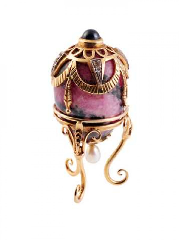 A rose quartz and 'jewelled' egg on stand, the metal testing as 14 carat gold, set with a cabochon sapphire, diamonds and a pearl drop, raised on a stand with three S-scroll legs. 5cm