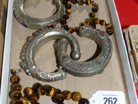 Two strings of tigers eye beads and three white metal bangles set with...
