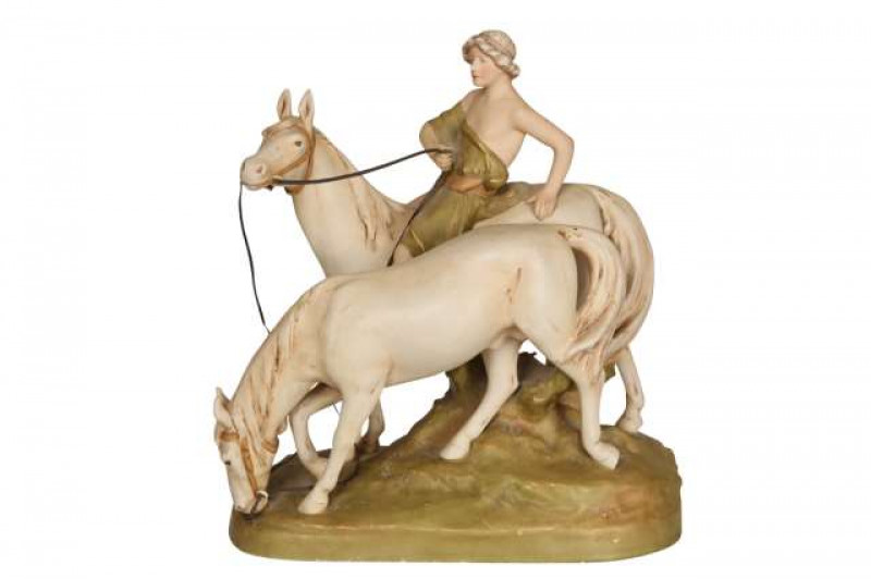 A Royal Dux model of a young man riding a horse, the bare foot rider with green robe, the horse standing with ears pricked, the second horse on halter with head down feeding, all standing on a grassy knoll, no. 2072, applied pink triangle mark. 34cm high