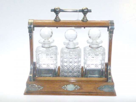 Oak and silver plated three bottle tantalus with ceramic label