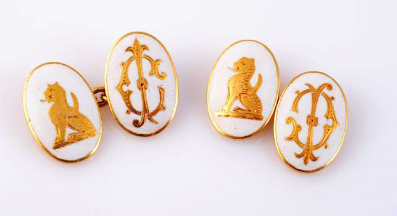 A PAIR OF GOLD AND ENAMEL CUFFLINKS c.1900-20 Each oval plaque of textured white enamelling depicting to the centre in gold work an Egyptian Sphinx or Egyptian lettering, each plaque joined by an articulated oval link chain. In fitted Mappin and Webb box.