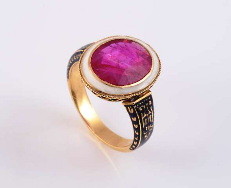 A VICTORIAN RUBY AND ENAMEL RING c.1870-80 The oval mixed cut ruby collet set within an open pierced detail mount set with a surround of white enamel, between moulded tapering shoulders set with delicate blue enamel detailing, on a plain band.  Ring size 