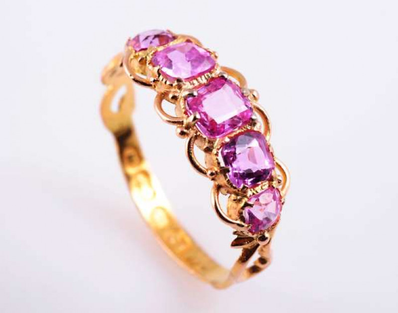 A PINK SAPPHIRE AND DIAMOND RING c.1880-90 The five graduating oval mixed cut pink sapphires claw set within an elaborate bead detail and curved metal work mount between moulded open scroll design shoulders on a heavily engraved and moulded band. Stamped 