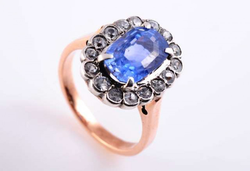 A SAPPHIRE RING c.1890-1900 The oval mixed cut sapphire four claw set within a scalloped edge surround set with sixteen old brilliant cut sapphires, all set in a heavily pierced detail mount between open pierced detail tapering shoulders on a plain band. 