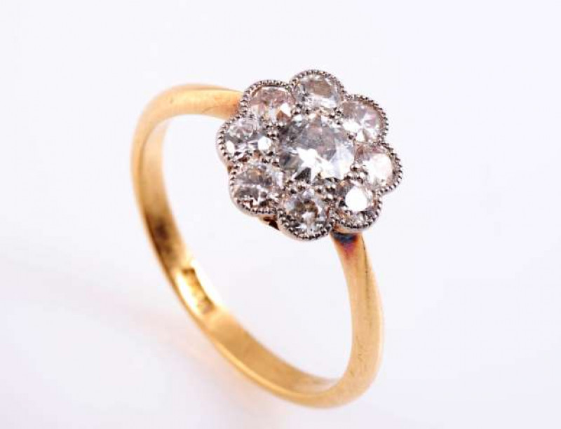 A DIAMOND RING c.1900 The old brilliant cut diamond eight claw set within a surround of eight old brilliant cut millegrain set diamonds, all set in an open pierced detail mount between tapering shoulders on a plain band. Stamped 18. Ring size M.  Weight a