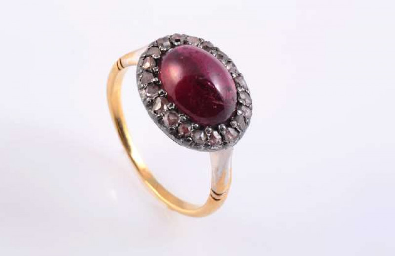 A GARNET AND DIAMOND RING c.1870-80 The oval cabochon cut garnet claw set within a surround of twenty rose cut diamond highlights, all set in an open mount with engraved detailing between slightly tapering shoulders with moulded detailing on a plain band.