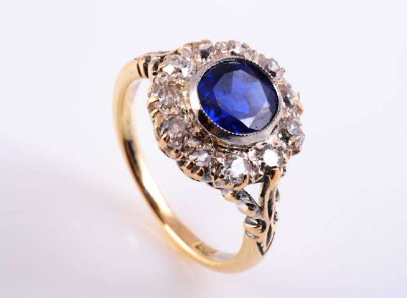 A BURMESE SAPPHIRE AND DIAMOND RING The round mixed cut sapphire collet set raised within a surround of eleven old brilliant cut claw set diamonds, all set in an open pierced detail mount, circa 1880, between open moulded leaf detail tapering shoulders on