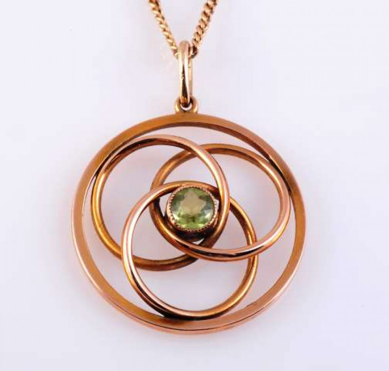A PERIDOT AND GOLD PENDANT c.1890 The round cut peridot millegrain set to the centre of three interlinked concentric circles, all enclosed within an open circular mount, suspending on a single articulated oval bale from a fine curb link chain with bolt ri