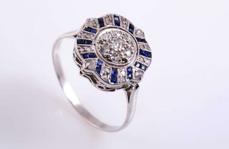 A SAPPHIRE AND DIAMOND RING c.1920 The seven old brilliant cut claw set diamonds set in a cluster in a circular mount within a surround of eight pairs of rose cut diamond highlights, alternately set with twelve pairs of square cut collet set sapphire high