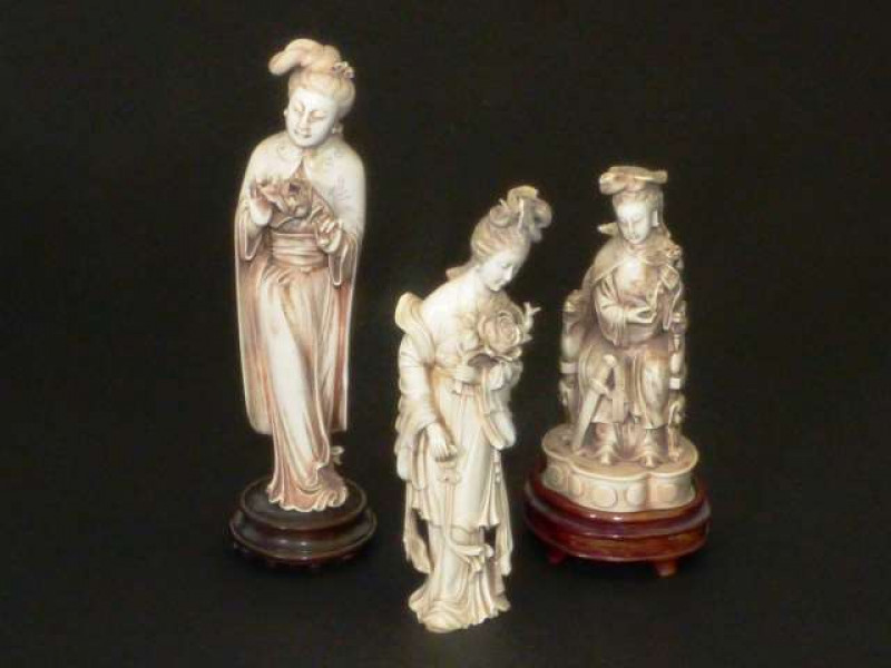 A GROUP OF THREE CHINESE IVORY FIGURES Probably late 19th/early 20th Century Each carved as a woman in flowing robes, the two standing figures holding flowers. Tallest excluding stand 25cm