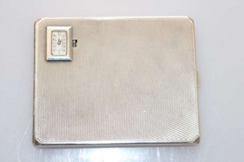 A GEORGE V SILVER CIGARETTE CASE WITH INSET WATCH, Smith & Bartlam, Birmingham 1930, the engine-turned case inset to one corner with a rectangular-faced watch with Arabic numerals. 5oz, 10.5cm by 8.5cm