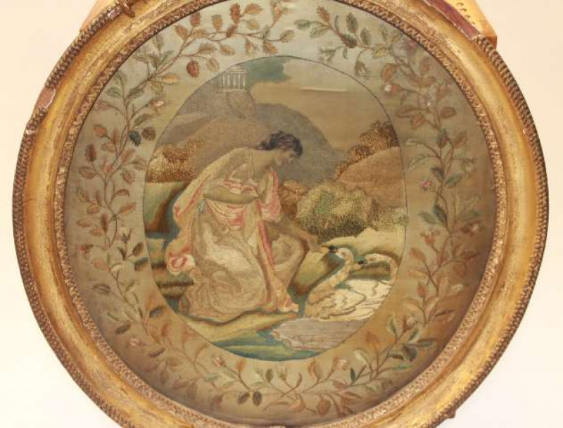 A GEORGE III SILKWORK PICTURE, slightly oval, of a lady feeding two swans in a landscape, in a gilt gesso frame. Overall 50.5cm