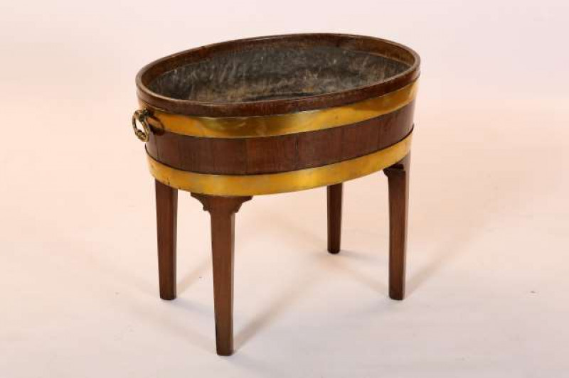 A GEORGE III BRASS-BOUND MAHOGANY OVAL WINE COOLER, with brass carrying handles and twin brass bands, lead lined, raised on a later stand. 59cm by 70cm by 48.5cm