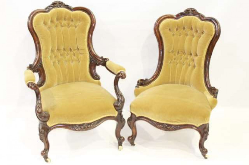 A PAIR OF 19TH CENTURY ROSEWOOD AND UPHOLSTERED SALON CHAIRS, lady's and gentleman's, each waisted and deep buttoned back with a lobed top rail centred by a scrolling foliate carving, above a stuffed over seat with serpentine front rail, the gentleman's i