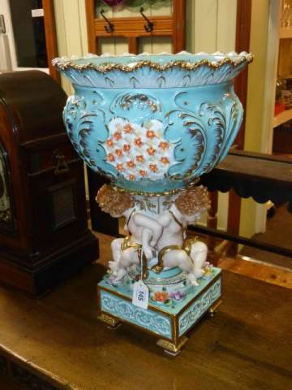 Continental porcelain centrepiece modelled as three cherubs supporting a pierced bowl on a floral encrusted square four footed base, 48cm high