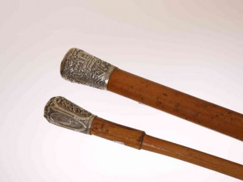 TWO WALKING STICKS WITH CHINESE WHITE METAL HANDLES, the first decorated...
