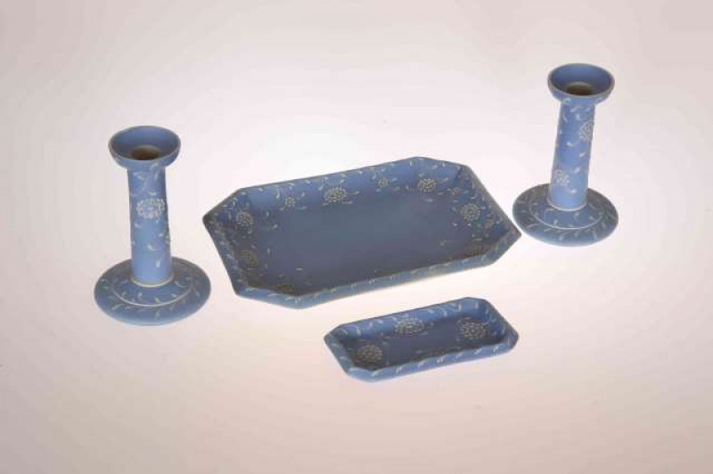A WEDGWOOD BLUE JASPER DRESSING TABLE SET BY HARRY BARNARD (1862-1933), comprising pair of candlesticks, tray and trinket dish, decorated in white slip with stylised flowers, signed, impressed factory marks. Tray 26.5cm by 19cm  Note: Barnard was born in 
