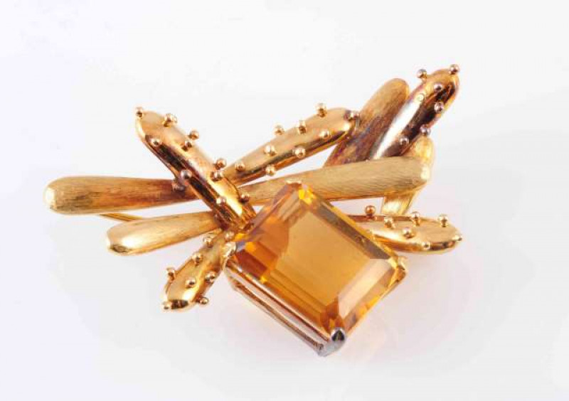 A CITRINE BROOCH, CIRCA 1950, the large square cut citrine four claw set within an abstract surround of ten moulded detail tapering oval mounts with brushed metal and beaded detailing, on a brooch pin fitting. Length approximately 5cm. Weight 18.5gms.