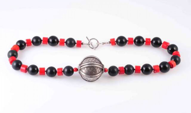 A CORAL AND BLACK BEAD NECKLACE, the eighteen black beads alternately strung with eighteen coral rounded beads, set to the front with a large textured metal silver coloured rotating bead, all strung onto a T bar fastening. Fastening stamped 925. Total len