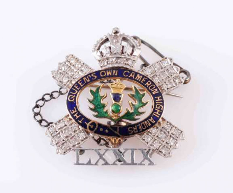 A DIAMOND AND ENAMEL BROOCH, set to the inside with a blue and green enamel thistle emblem, within a surround of blue enamelling and gold lettering 'The Queens Own Cameron Highlanders', in turn within a surround of a cross design mount set throughout with