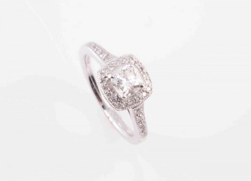 A DIAMOND AND PLATINUM RING, the cushion cut diamond four claw set within a bezel of twenty brilliant cut claw set diamond highlights in an open mount between open shoulders each set with five graduating brilliant cut diamond highlights, on a plain band. 