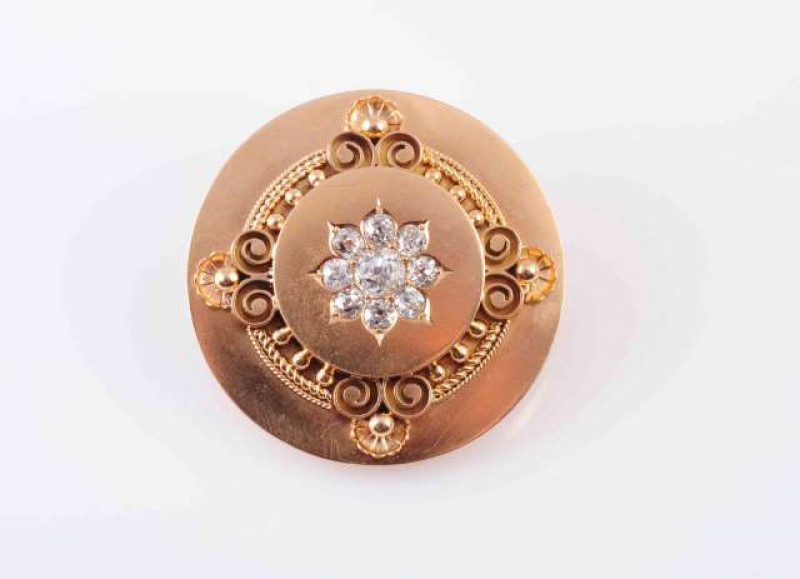 A DIAMOND BROOCH, CIRCA 1880, the round mixed cut diamond claw set within a surround of eight smaller round mixed cut diamonds in engraved leaf shaped mounts, set to the centre of a raised circular mount, in turn within elaborate scroll, beaded and rope w