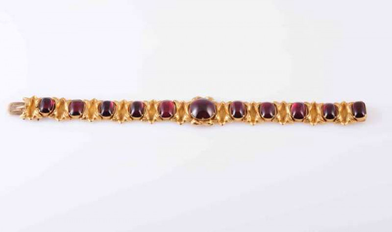 A GARNET SET BRACELET, circa 1880-1890, the round cabochon cut garnet claw and collet set within a moulded leaf detail mount, between ten oval cabochon cut garnets each collet set, alternately spaced with moulded leaf detail and brushed metal links, each 