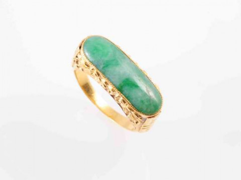 A JADEITE RING, the oval jadeite plaque set in a heavy closed back mount...