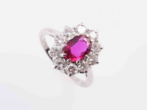 A RUBY AND DIAMOND RING, the oval cut ruby ten claw set within a surround...