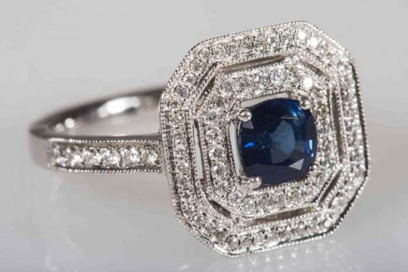 A SAPPHIRE AND DIAMOND RING, the cushion mixed cut sapphire four claw set within an inner surround of brilliant cut claw set diamond highlights, in turn within an outer surround of  brilliant cut claw set diamond highlights, all set in an open pierced det