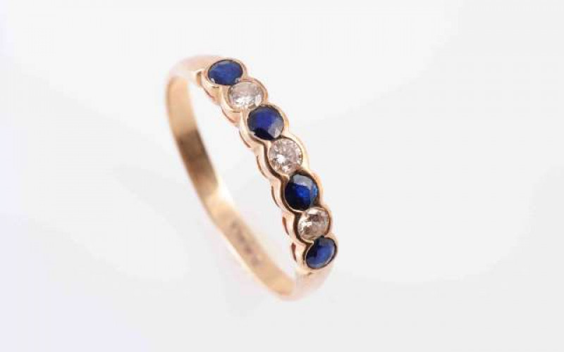 A SAPPHIRE AND DIAMOND RING, the four round cut sapphires alternately spaced with three brilliant cut diamonds, all collet set in a scalloped edge mount between tapering shoulders on a plain band. Stamped 375. Ring size Q 1/2. Weight 1.6gms.
