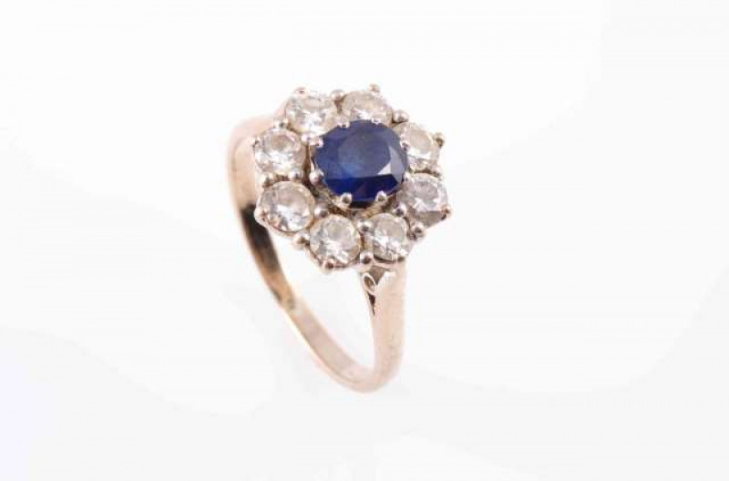 A SAPPHIRE AND DIAMOND RING, the round cut sapphire eight claw set within a surround of eight brilliant cut claw set diamonds, all set in a raised pierced detail mount between pierced tapering shoulders on a plain band. Stamped 18. Ring size K. Weight 3.8