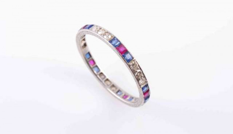A SAPPHIRE, RUBY AND DIAMOND ETERNITY RING, the five sets of three brilliant cut diamond highlights alternately and evenly spaced by five sets of a single square cut ruby highlight between two square cut sapphire highlights, all set between a subtly engra