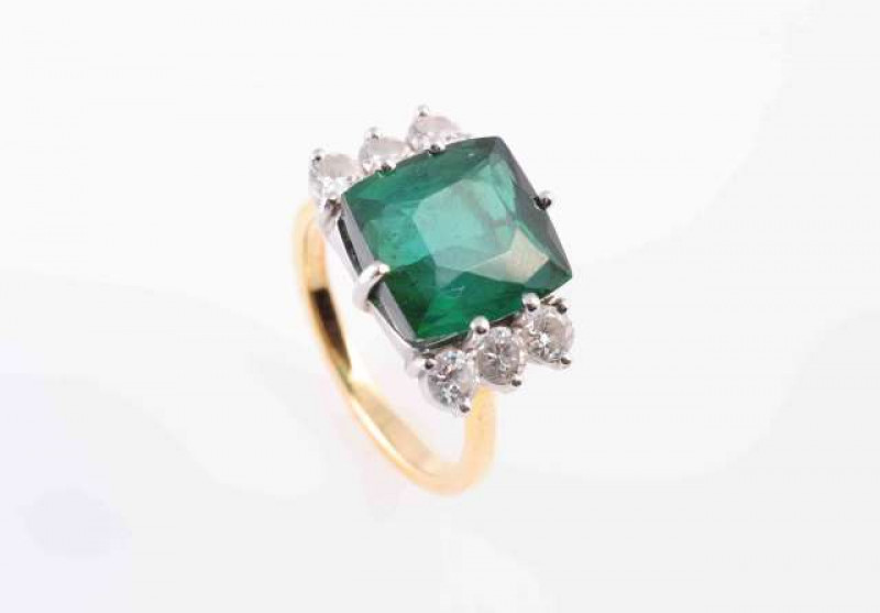 A TOURMALINE AND DIAMOND RING, the square cushion cut green tourmaline six claw set between six brilliant cut claw set diamonds, all set in a raised open detail mount between pierced tapering shoulders on a plain band. Stamped 18CT. Ring size J 1/2. Weigh