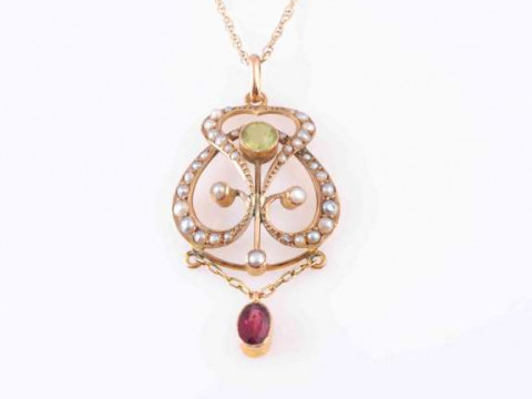 AN ART NOUVEAU PERIDOT, GARNET AND SEED PEARL PENDANT, the oval cut collet...