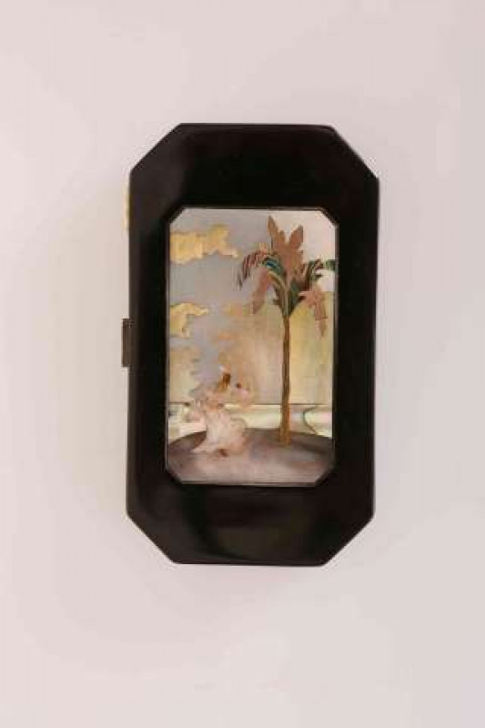A FRENCH SILVER GILT AND BLACK ENAMEL COMPACT, CIRCA 1920'S, inlaid with mother of pearl, depicting an eastern gentleman by a palm tree, enclosing two hinged compartments and an extending lipstick case, mirror to the underside of the cover. 8.5cm by 5cm