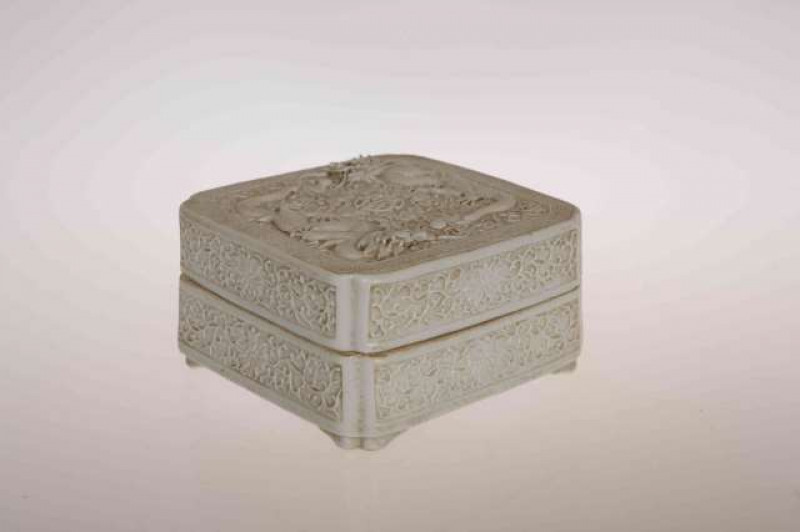 A CHINESE PORCELAIN BOX AND COVER, square with inverted corners, moulded with dragons and pearls, impressed seal mark. 9cm by 9cm