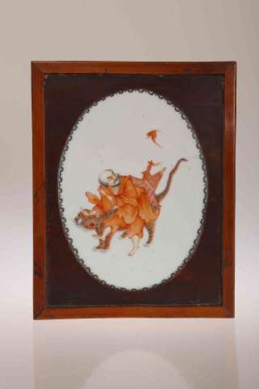 A CHINESE PORCELAIN PLAQUE, oval, painted with a street vendor on the back of a tiger with a bat overhead, in a wooden mount and frame. Oval 18.5cm by 13.5cm