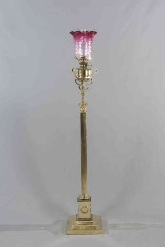 A LATE 19TH CENTURY BRASS CORINTHIAN COLUMN STANDARD LAMP, with stepped square base and tinted cranberry shade. 174cm